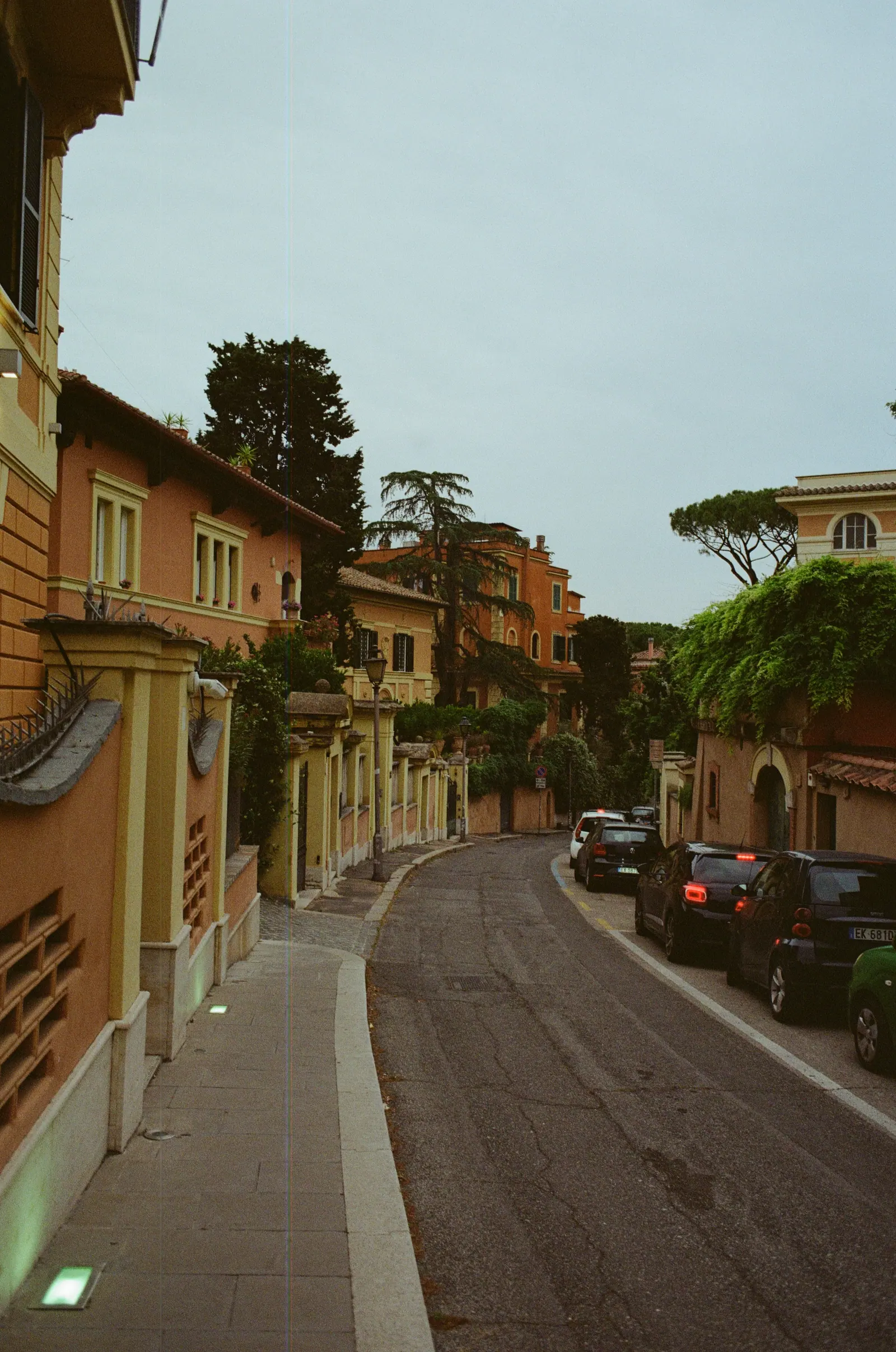 A quiet street curving between ochre villas and umbrella pines, cars parked along the kerb.