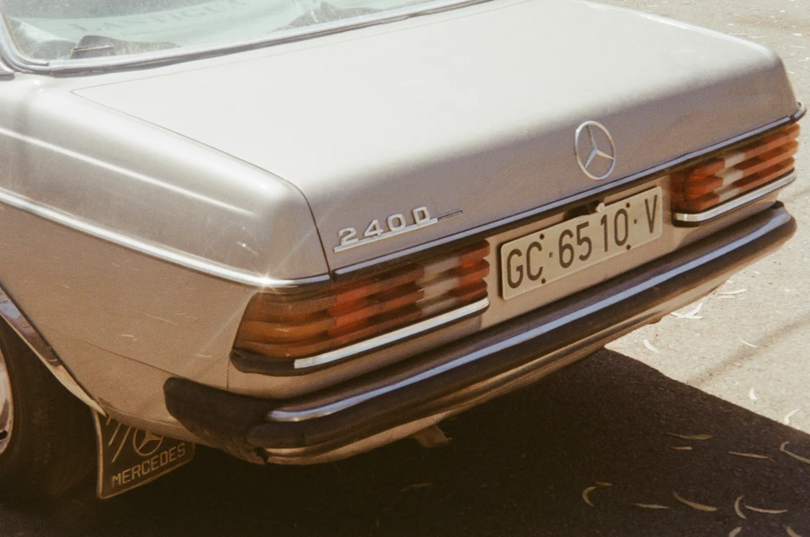 Close view of the rear of a silver Mercedes 240 D in bright sun.