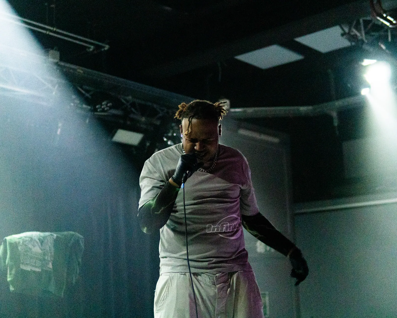 A performer in white sings under stage spotlights, a towel draped over the monitor beside him.