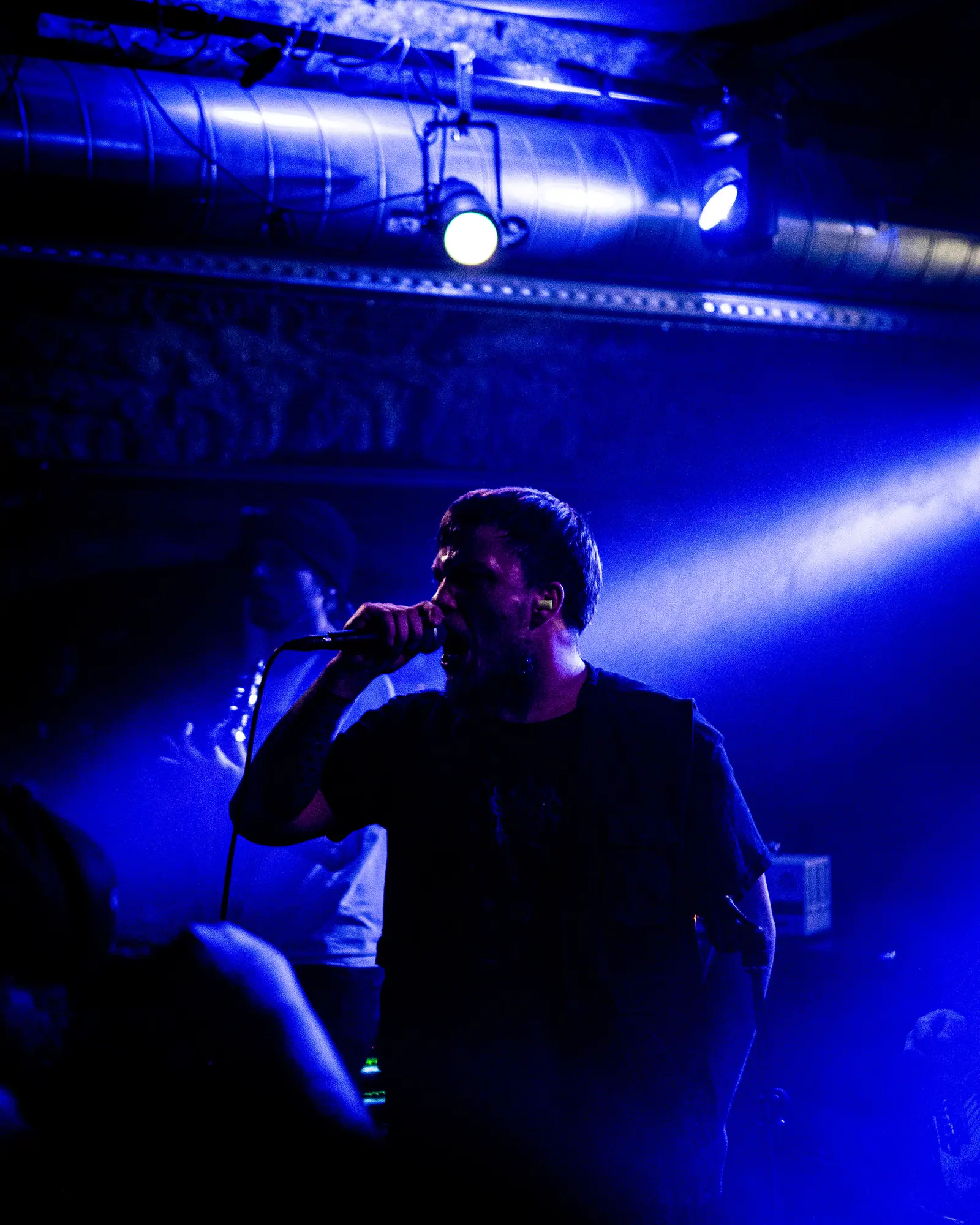 A vocalist sings into a microphone, backlit by a blue spotlight.
