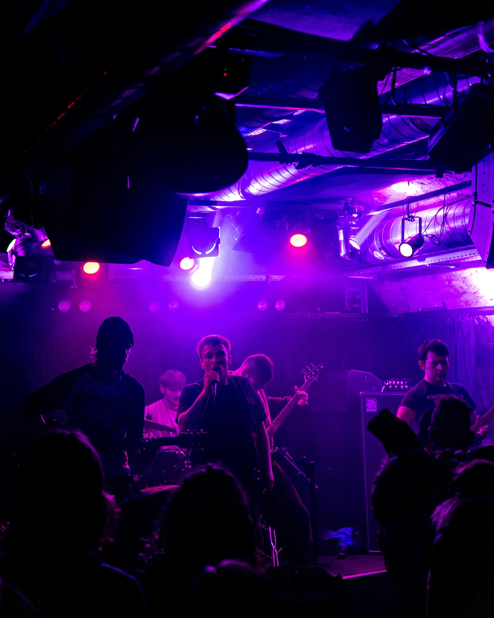 A band plays on a stage washed in purple light, seen from within the crowd.