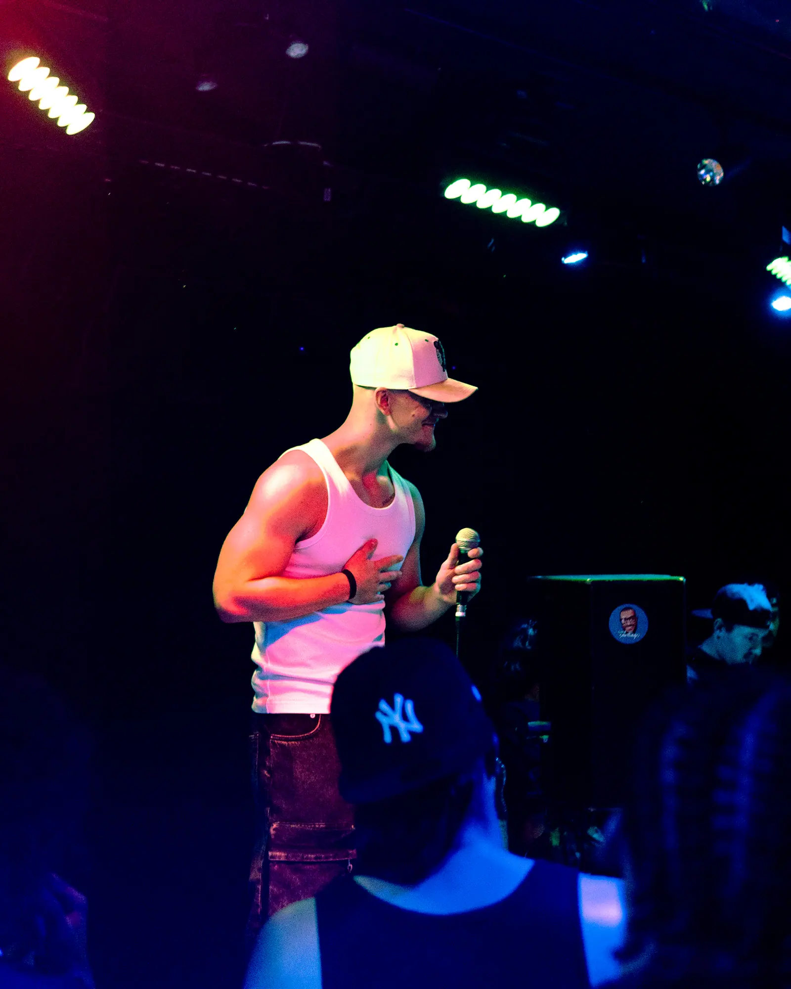 The performer holds a hand to his chest as he talks to the crowd, a fan in a New York cap in the foreground.