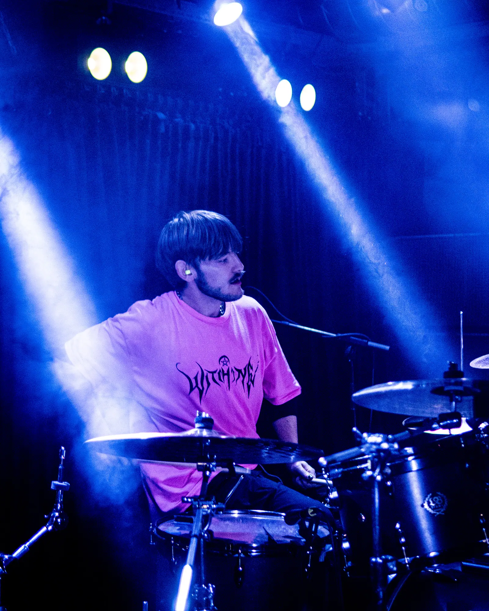 A drummer plays under blue stage beams.