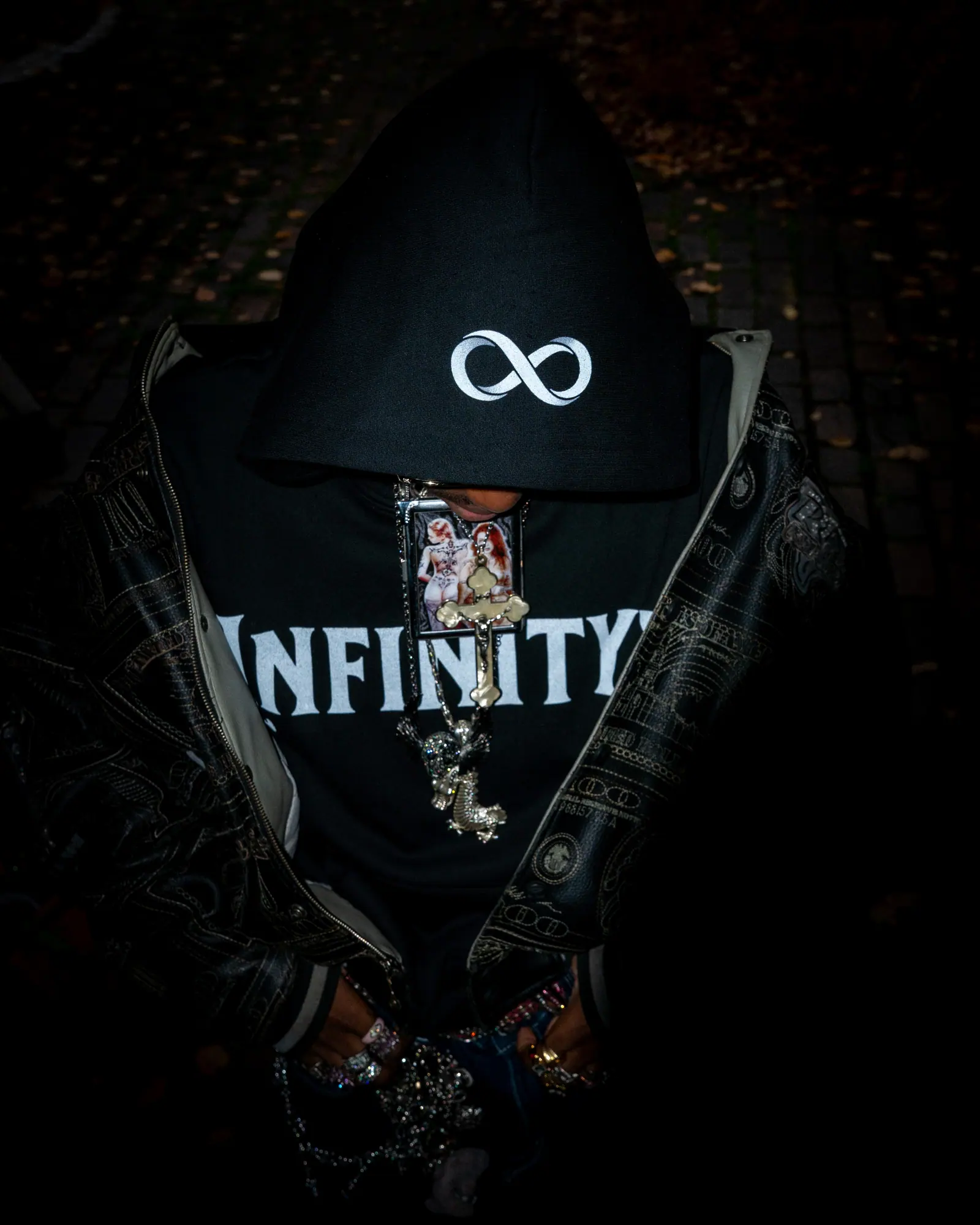 Low-key close portrait of a hooded figure in a black Infinityy hoodie, an infinity symbol on the hood and the face lost in shadow.