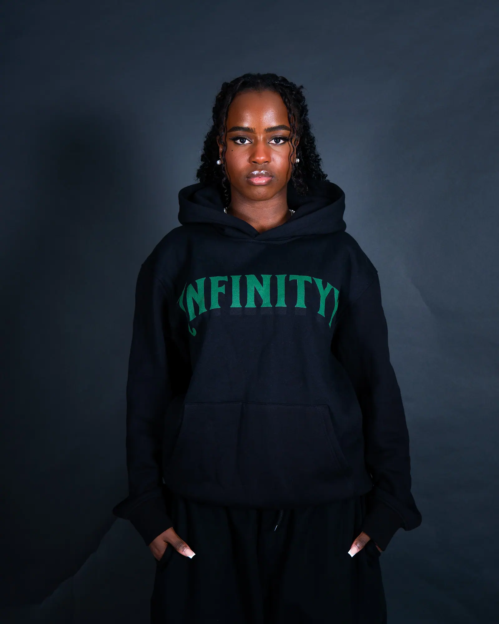 A woman in a black hoodie with green Infinityy lettering looks into the camera.
